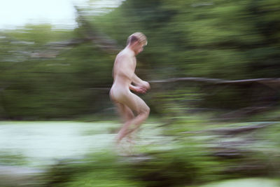 Blurred motion of sensuous naked man running over lake in forest