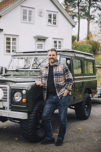 Mature man with hand in pocket standing by sports utility vehicle