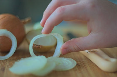 Cropped hand holding onion ring on cutting board