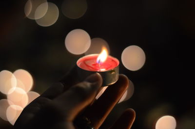 Close-up of hand holding tea light candle against black background