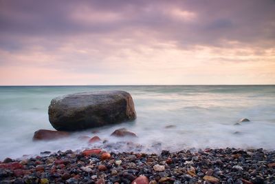  big boulders sticking out from smooth wavy sea. pink horizon with first hot sun style toned effect