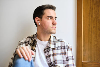 Portrait if a young man chilling at home looking away while listening music with earphones.