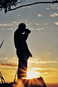 Silhouette man photographing against sky during sunset