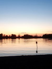 Silhouette man on lake against sky during sunset