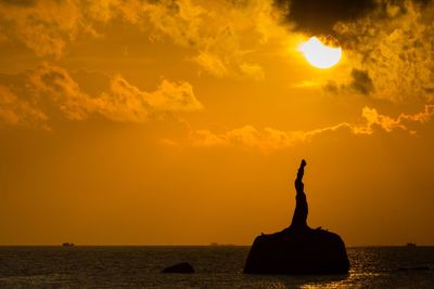 Silhouette sculpture by sea against orange sky