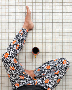 High angle view of woman sitting on white tiled floor at home with cup of coffee