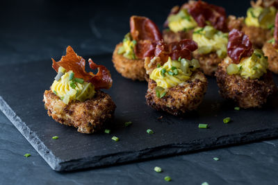 Gourmet deep fried deviled eggs garnished with chives and fried prosciutto