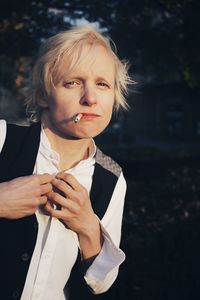 Portrait of beautiful young woman smoking cigarette against trees