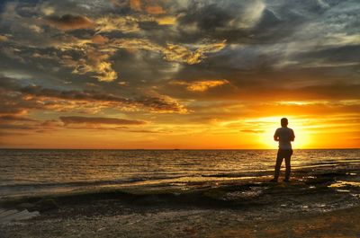 Rear view man standing at beach against sky during sunset