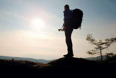 Silhouette man standing on rock against sky during sunset