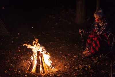 Man sitting by bonfire in forest at night