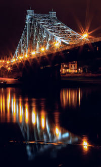 Illuminated bridge over river against sky at night