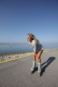 Full length of woman inline skating on road by sea against clear sky