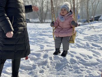 Cute girl sitting on swing outdoors during winter