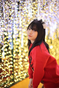 Portrait of young woman standing against illuminated christmas tree