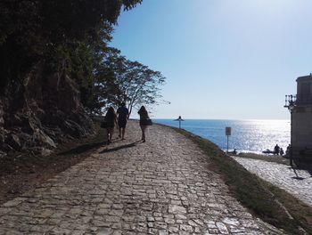 Rear view of people walking by sea against sky