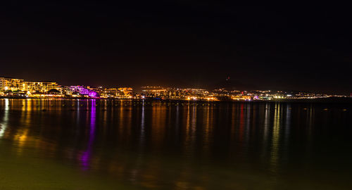 Illuminated buildings by river against sky at night