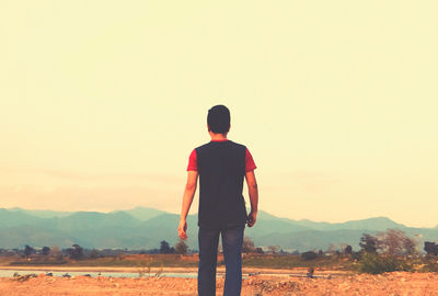 Rear view of man standing on field against sky