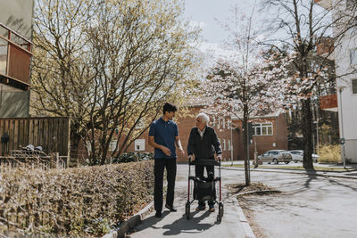 Male care assistant talking to senior man with walker on sidewalk