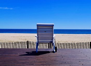 Deck chairs on beach against clear blue sky