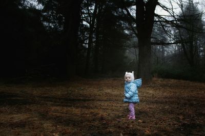 Side view of cute baby girl wearing warm clothing standing on field in forest