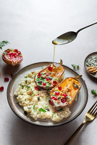 From above of olive oil pouring on homemade roasted pumpkins with pomegranates seeds served on plate with rice on table in light kitchen