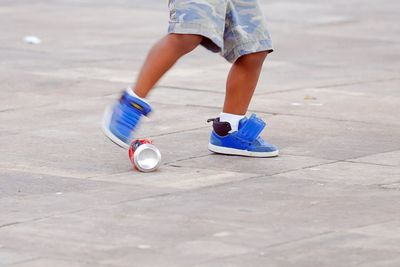 Low section of boy kicking can on footpath