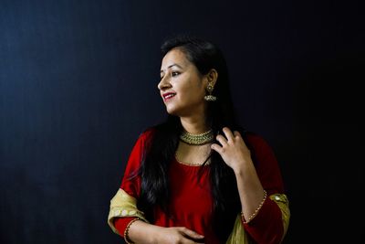 Young woman looking away while standing against black background