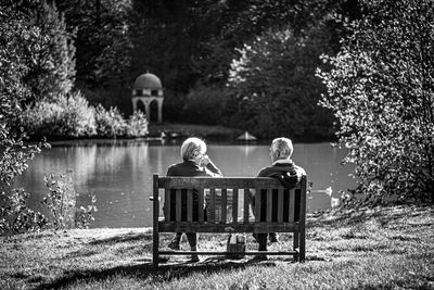 Rear view of couple sitting on bench by lake
