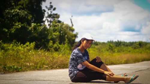 Portrait of smiling young woman sitting on road against trees