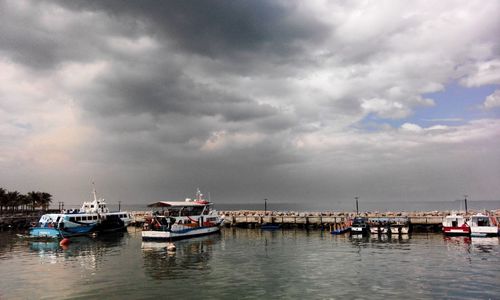 Boats in calm sea against cloudy sky