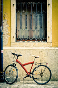 Bicycle parked on sidewalk against window