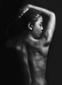 Rear view of shirtless woman against black background