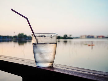 Close-up of water in glass on table against lake