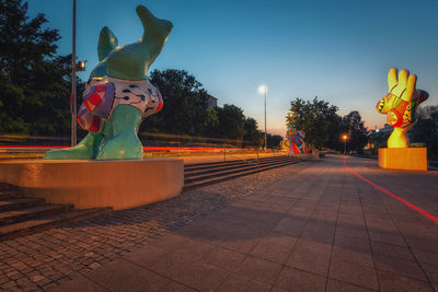 Statue by illuminated footpath against sky