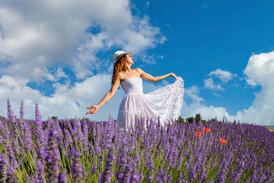 Young woman with long brown hair singing and dancing in a lavender field. 