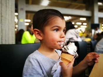 Cute boy eating ice cream cone while sitting on chair at restaurant