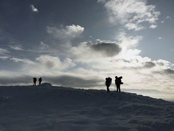 Low angle view of silhouette hikers standing on snowcapped mountain against sky