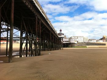 Pier over beach by buildings against sky