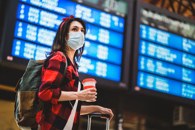 Young woman wearing mask looking away while standing at airport