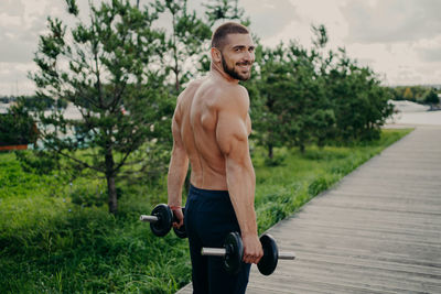 Portrait of shirtless man lifting dumbbells in park