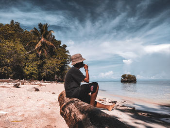 Man sitting on rock by sea against sky