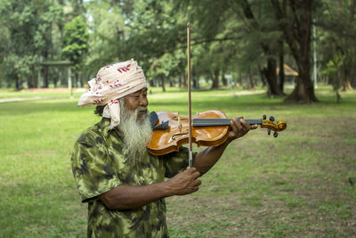 Bearded man playing violin against trees