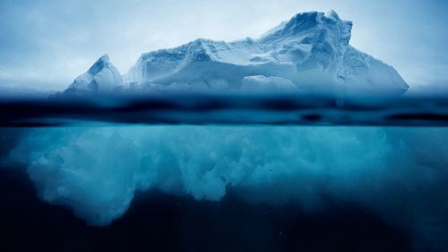 Iceberg floating on sea against sky