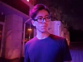 Portrait of young man standing against illuminated light at night