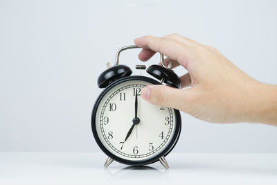 Close-up of hand holding clock over white background