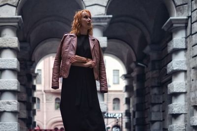 Low angle view of woman wearing jacket while standing against arch