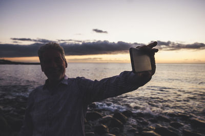 Man photographing from mobile phone at beach during sunset