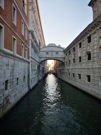Arch bridge over canal amidst buildings against sky in city