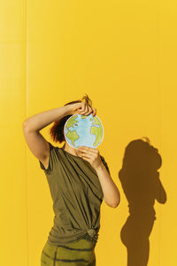 Rear view of woman with umbrella standing against yellow wall